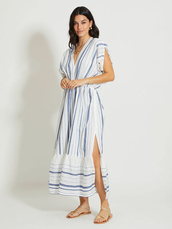 Woman Standing Wearing lemlem LEILA | Plunge Dress featuring crisp white fabric woven with diagonal dotted stripes in bright blue and a subtle textured weave
