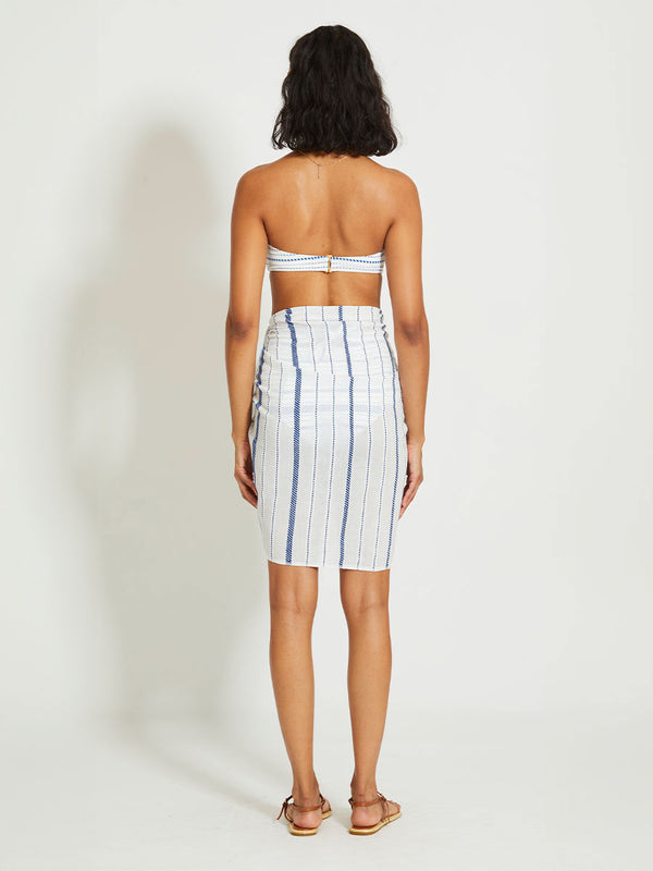 Back of a Woman Standing Wearing lemlem LEMA | Sarong featuring crisp white fabric woven with diagonal dotted stripes in bright blue and a subtle textured weave