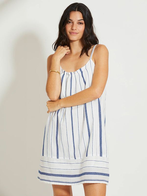 Woman Standing Wearing lemlem ZINA | Swing Dress featuring crisp white fabric woven with diagonal dotted stripes in bright blue and a subtle textured weave