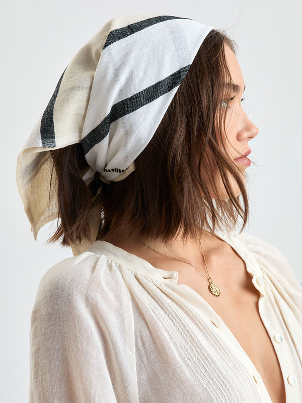 Woman standing wearing lemlem handwoven DANA Bandana featuring  refined palette of crisp white, soft cream, and deep black and white jeans along with cream handwoven MITA Blouse