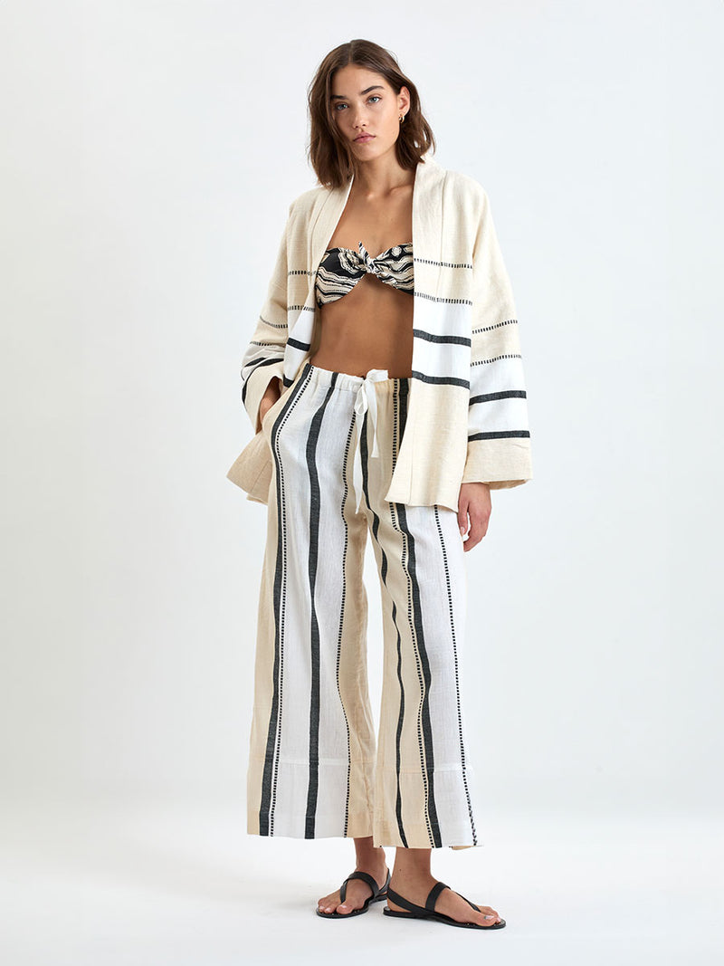 Woman standing wearing lemlem handwoven TERARA Jacket and DESTA Pants  featuring  refined palette of crisp white, soft cream, and deep black