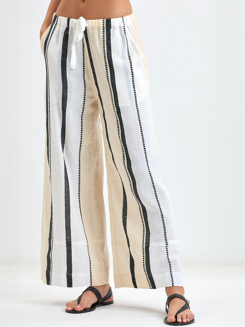 Close up on Woman's legs standing wearing lemlem handwoven DESTA Pants  featuring  refined palette of crisp white, soft cream, and deep black