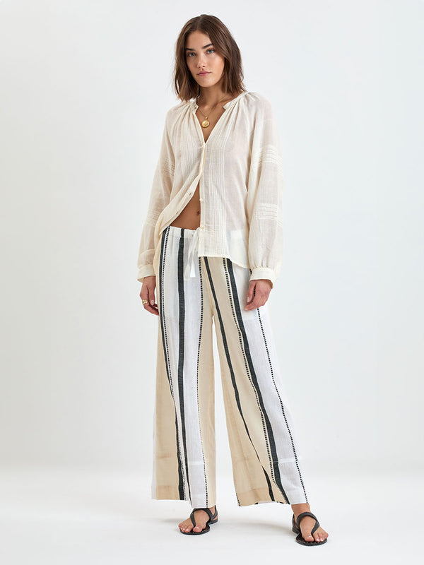 Model standing wearing lemlem handwoven DESTA Pants  featuring  refined palette of crisp white, soft cream, and deep black and beige MITA Blouse
