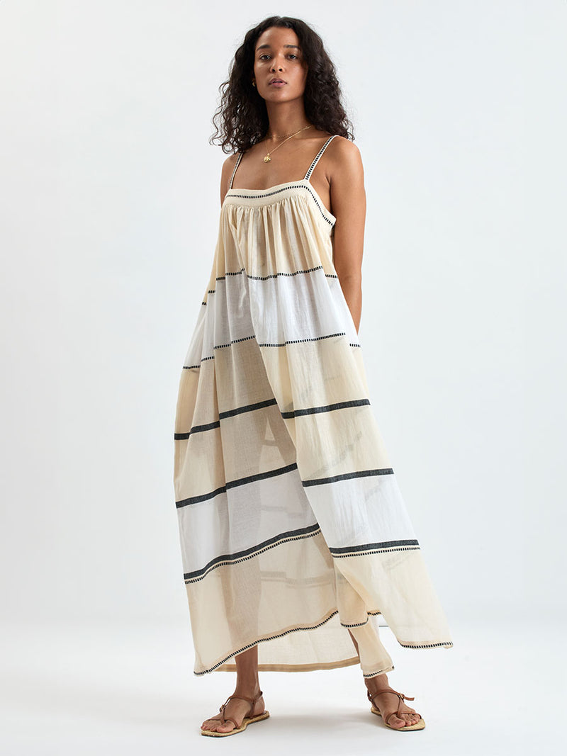 Woman standing wearing lemlem handwoven EDA Dress featuring  refined palette of crisp white, soft cream, and deep black