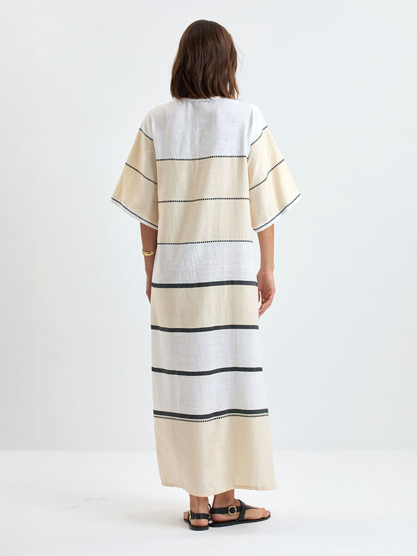 Back of a Woman standing wearing lemlem handwoven EDNA Dress featuring  refined palette of crisp white, soft cream, and deep black