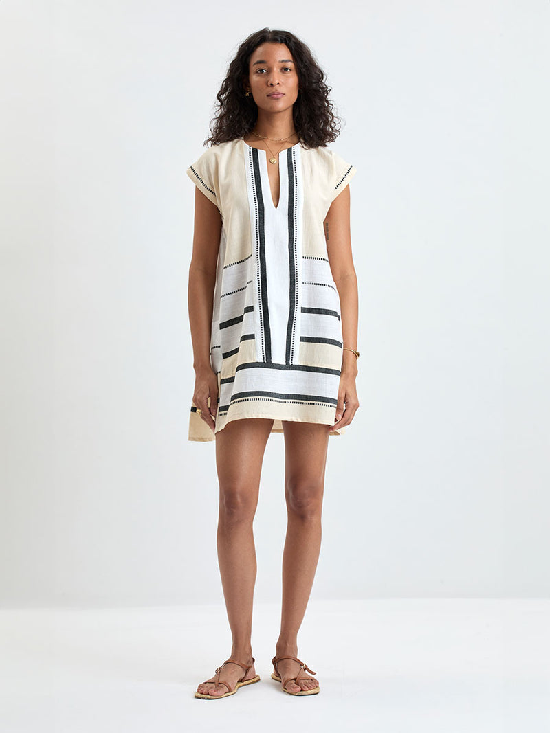 Woman standing wearing lemlem handwoven ELINA Caftan featuring  refined palette of crisp white, soft cream, and deep black