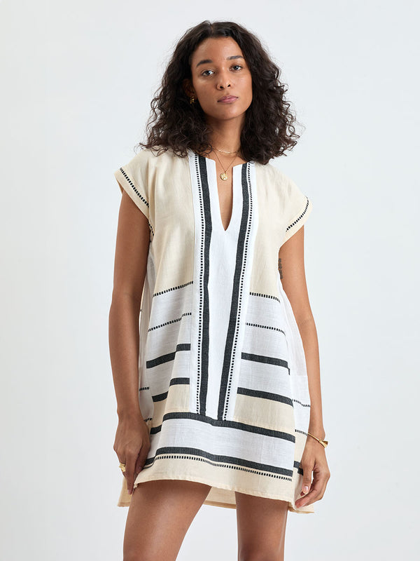 Woman standing wearing lemlem handwoven ELINA Caftan featuring  refined palette of crisp white, soft cream, and deep black