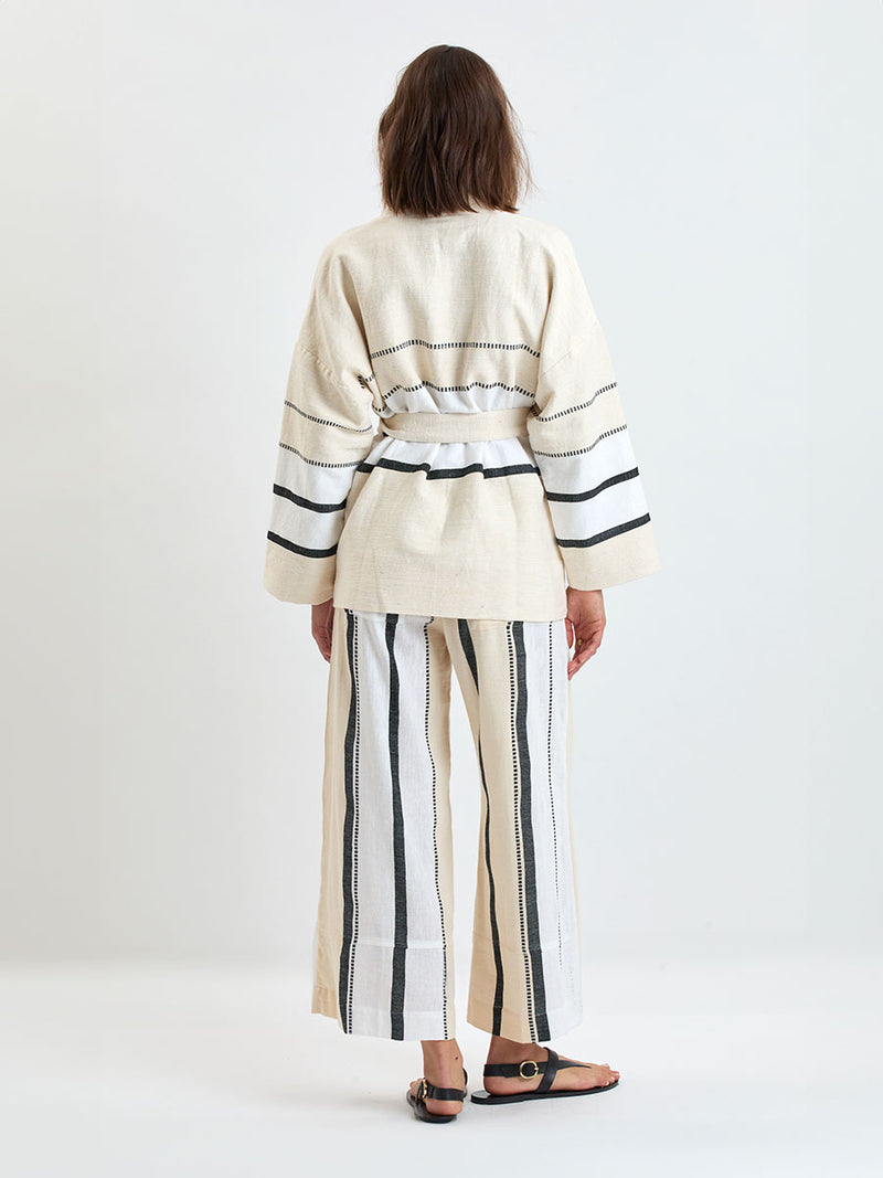 Back of a Woman standing wearing lemlem handwoven TERARA Jacket and DESTA Pants  featuring  refined palette of crisp white, soft cream, and deep black