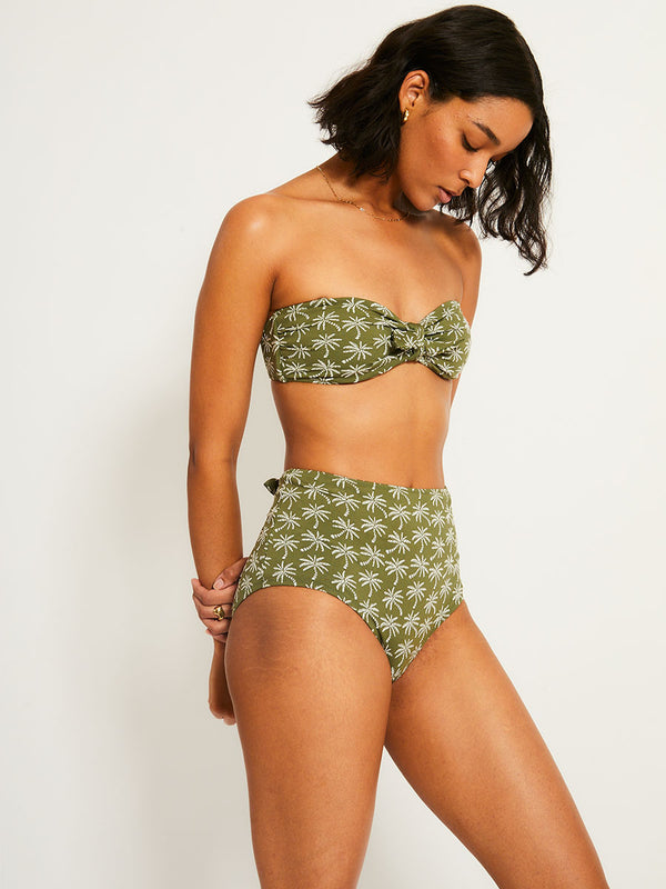 Side Shot of a Woman Standing Wearing lemlem bandeau top  featuring  jacquard fabric adorned with custom-designed knitted palm trees and matching high waist bottom