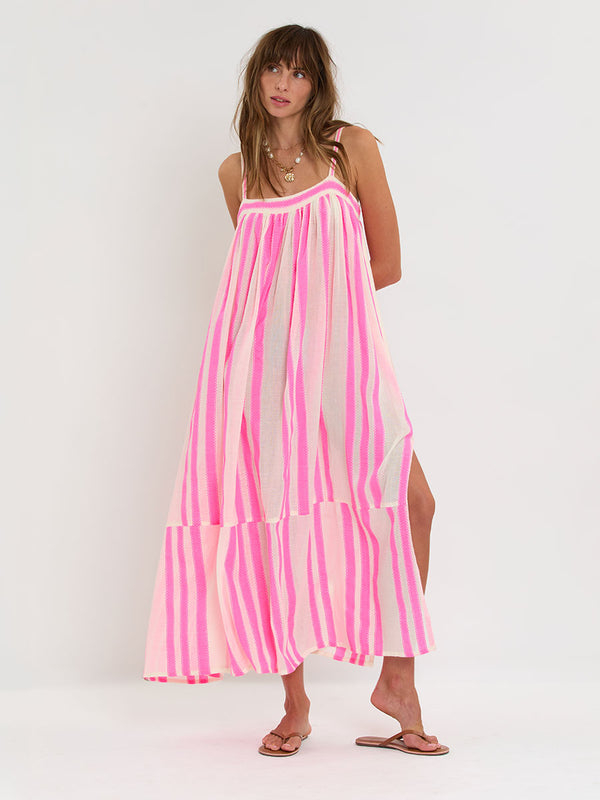 Woman Standing wearing lemlem handwoven EDA Slip Dress featuring a ribbon stripe pattern with a picot edge in vibrant neon pink on a soft vanilla background 