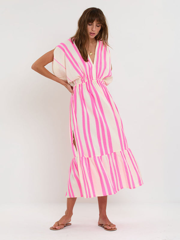 Woman Standing wearing lemlem handwoven LEILA Dress featuring a ribbon stripe pattern with a picot edge in vibrant neon pink on a soft vanilla background 