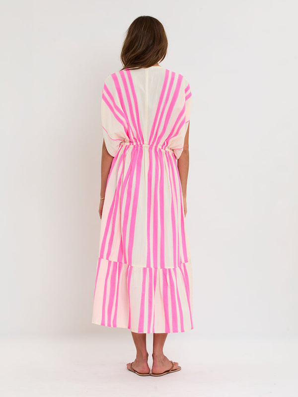 Woman Standing wearing lemlem handwoven LEILA Dress featuring a ribbon stripe pattern with a picot edge in vibrant neon pink on a soft vanilla background 