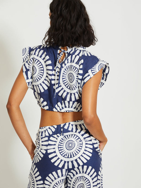 Back of a Woman Standing Wearing lemlem MUNA | Ruched Crop Top Featuring a bold geometric medallion pattern on navy background, inspired by traditional Tibeb motifs.
