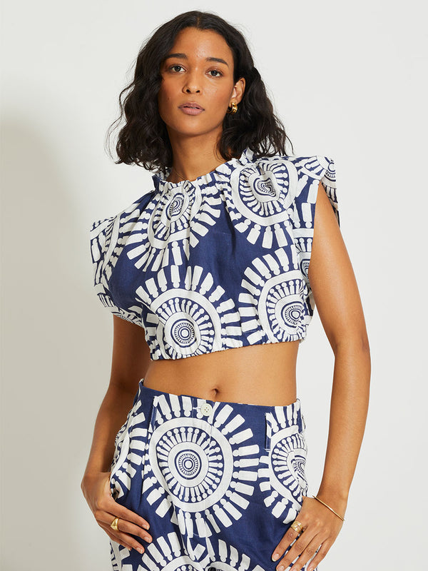 Woman Standing Wearing lemlem MUNA | Ruched Crop Top Featuring a bold geometric medallion pattern on navy background, inspired by traditional Tibeb motifs.