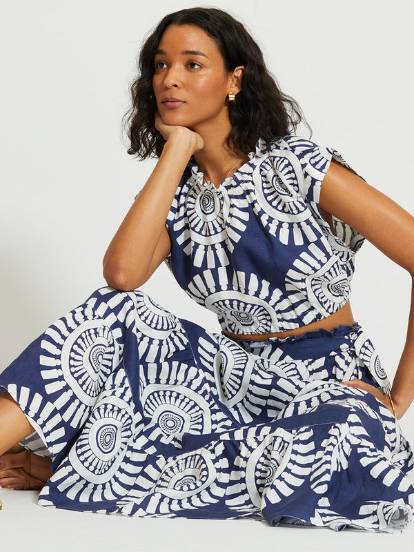 Woman Sitting Wearing lemlem MUNA | Ruched Crop Top Featuring a bold geometric medallion pattern on navy background, inspired by traditional Tibeb motifs.
