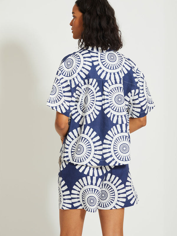Back of a Woman Standing Wearing lemlem TUULI | Cabana Shirt Featuring a bold geometric medallion pattern on navy background, inspired by traditional Tibeb motifs.