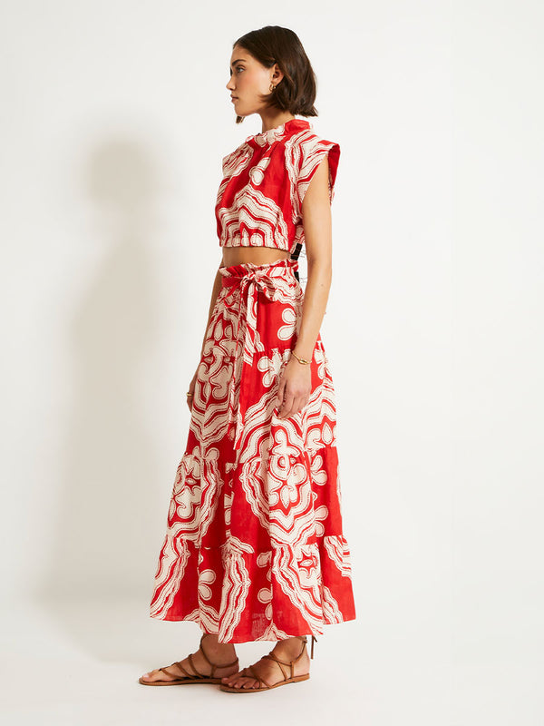 Side shot of a Woman Standing Wearing  lemlem Crop Top and Skirt featuring custom-designed print inspired by ancient architectural patterns in rich, vibrant red and creamy ivory colors