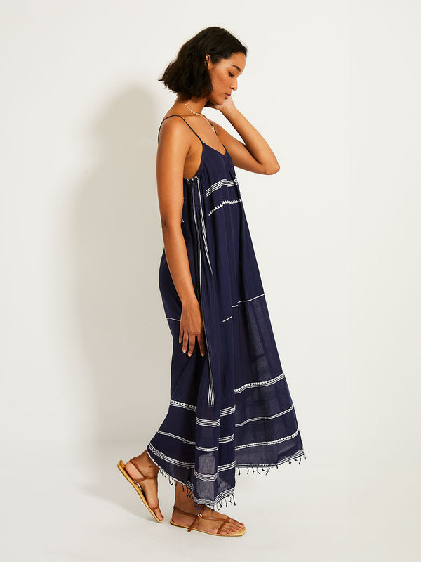 Side view of a woman standing wearing the Nunu Long Slip Dress in navy blue featuring white stripes and graphic lines.