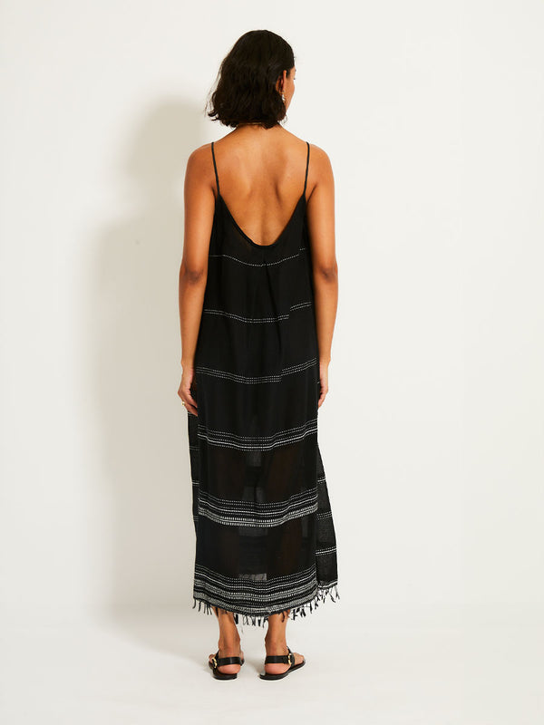 Back view of a woman standing wearing the Leliti Slip Dress in Black with white stitching allover.
