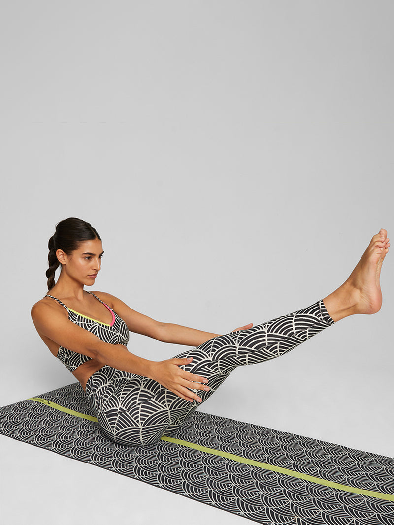 Woman Exercising on yoga mat wearing Puma x lemlem low impact bra in Ghost Pepper and Black colors featuring color pop green  and pink accents