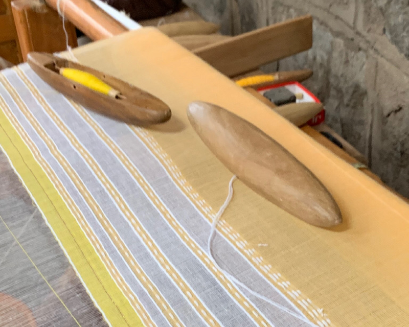 Yellow fabric being hand-woven on a loom with shuttles