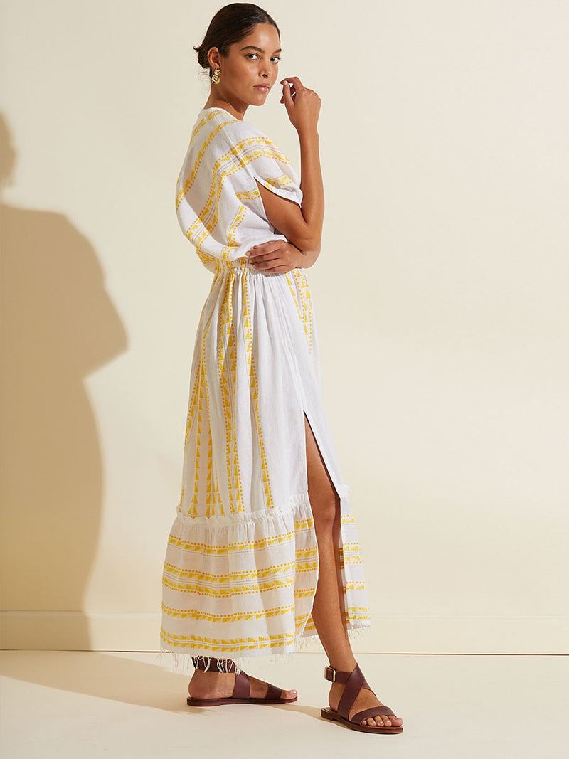 Side view of a woman wearing the Abeba Plunge Neck Dress featuring the yellow signature Tibeb pattern and gold lurex highlights on a white background.