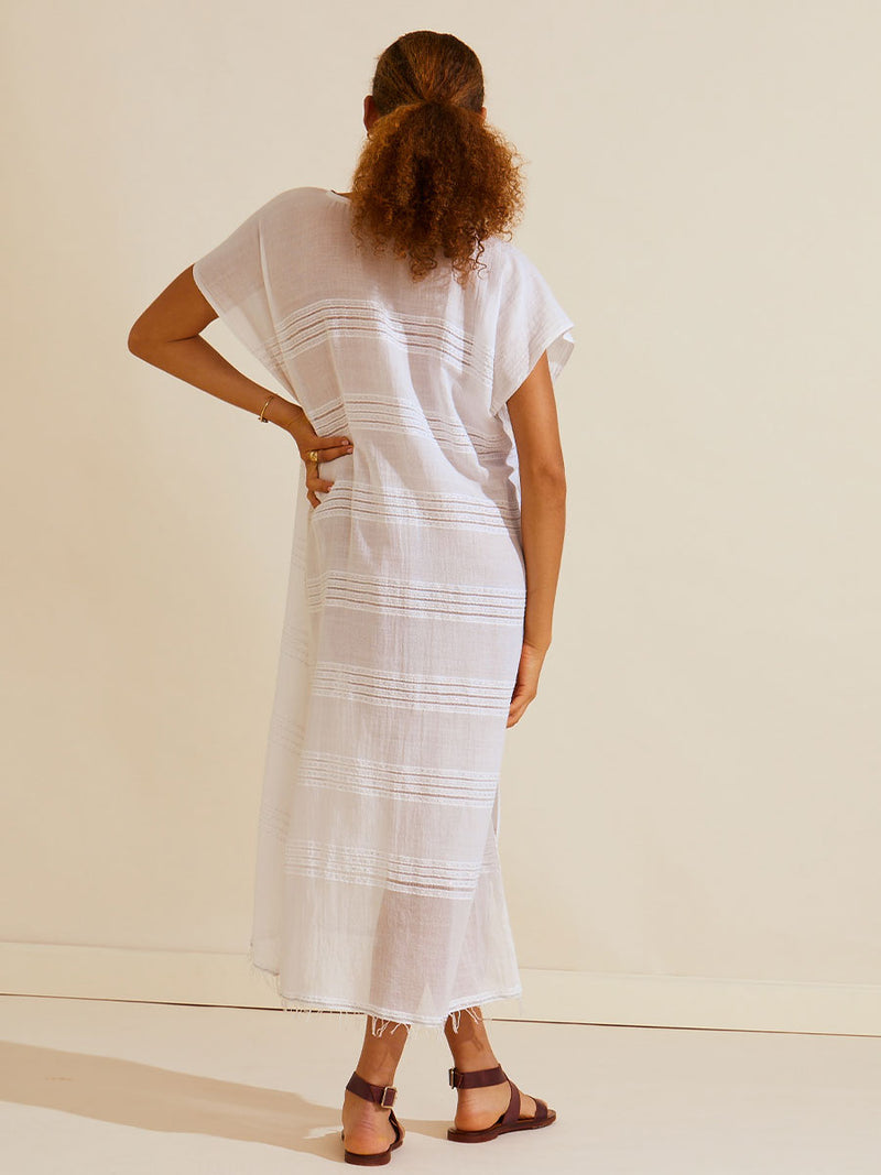 Back view of woman standing with her hand on her hipswearing a white Abira classic caftan with stitches of silver lurex