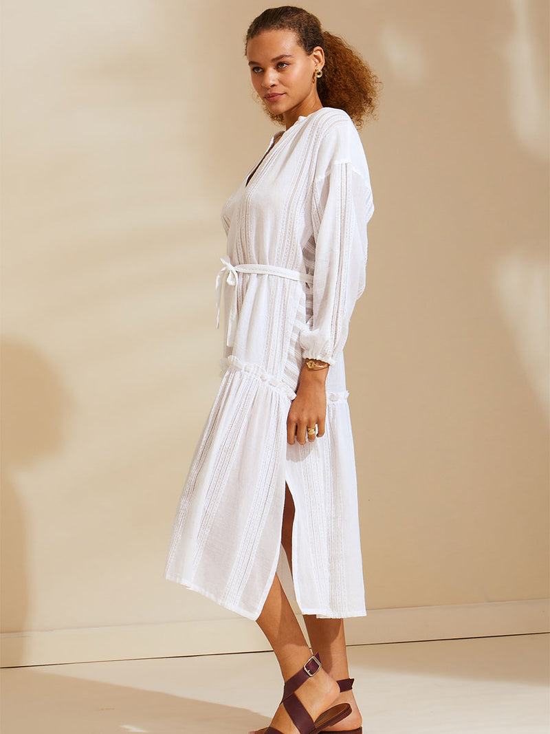 Side view of a woman standing wearing a white Abira Poet Shirt Dress with stitches of silver lurex