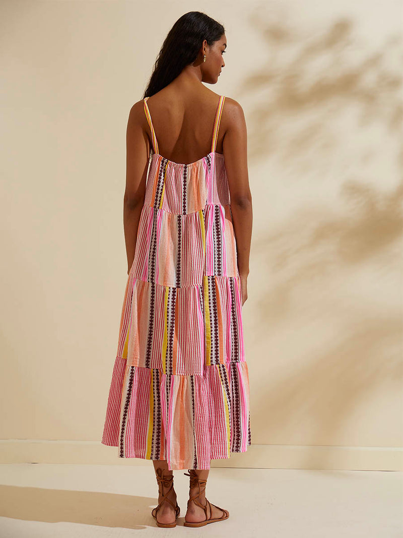 Back view of a woman standing wearing the Cirq Cascade Dress featuring pink, orange and yellow stripes and signature Tibeb design in burgundy bands.