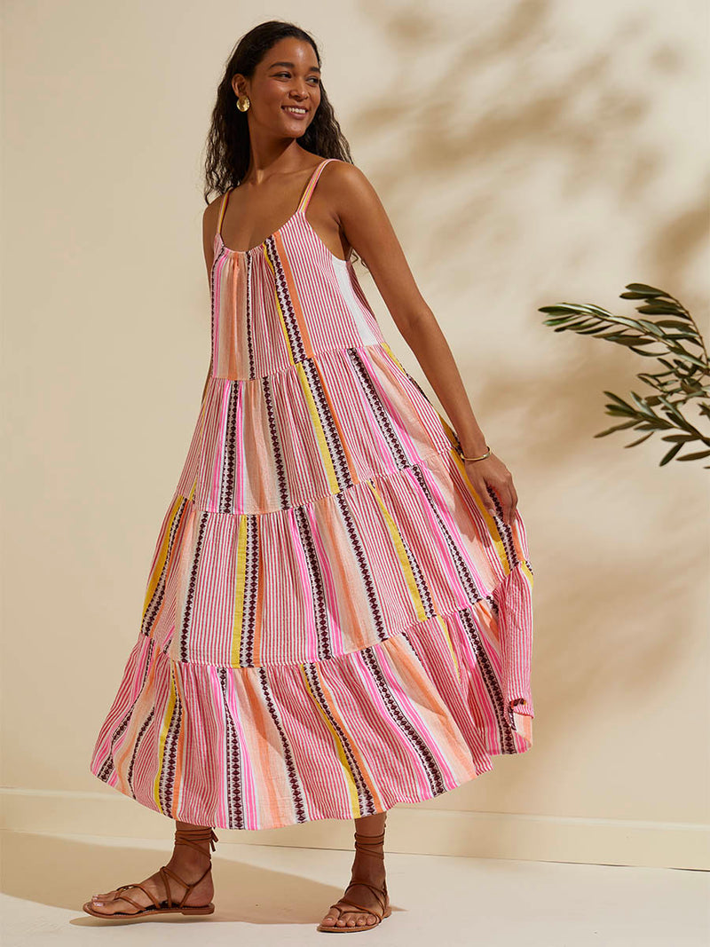 Woman standing wearing the Cirq Cascade Dress featuring pink, orange and yellow stripes and signature Tibeb design in burgundy bands.