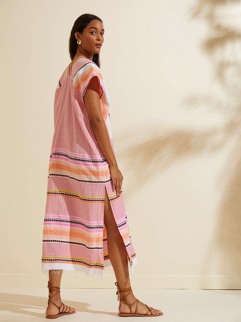 Back of a woman walking wearing the Cirq Long Caftan Dress featuring pink, orange and yellow stripes and signature Tibeb design in burgundy bands.