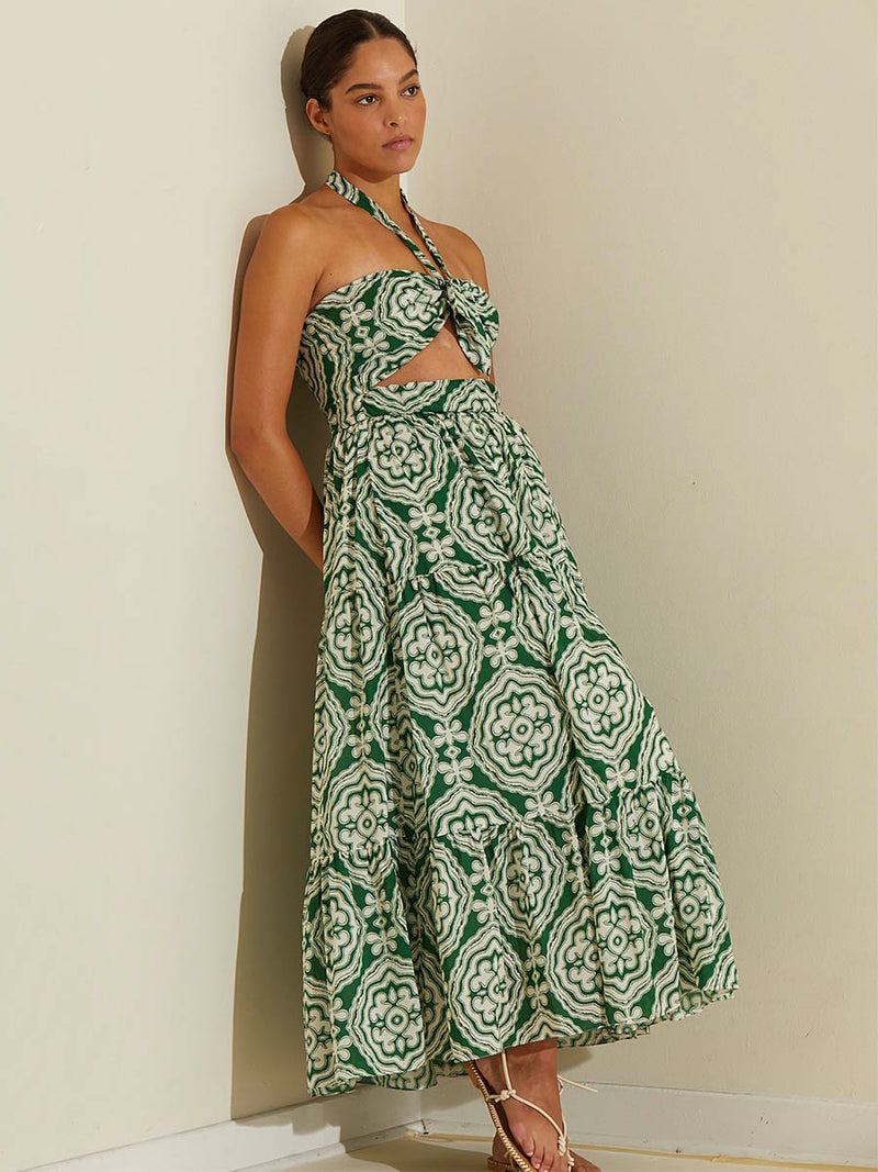 Woman standing wearing the Medallion Cutout Dress featuring architectural white patterns on a deep green background.