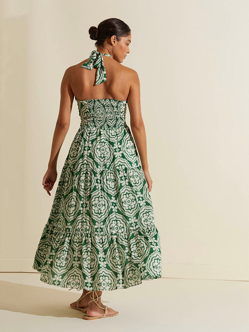 Back view of a woman walking wearing the Medallion Cutout Dress featuring architectural white patterns on a deep green background.