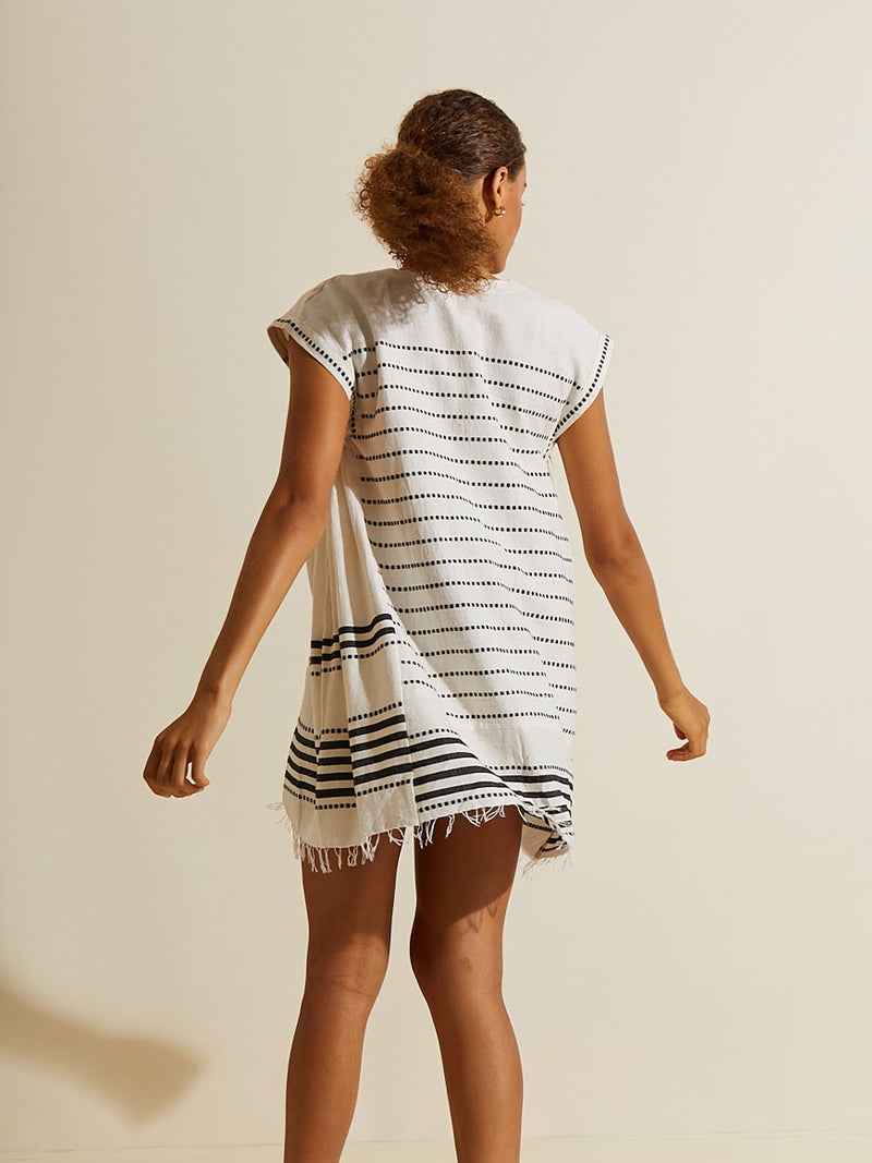 Back view of a woman twirling wearing the Eshe Caftan Dress featuring architectural and textured black stripes and dotted lines on an off white background.