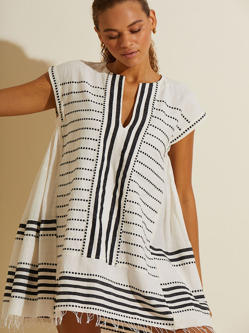 Woman standing wearing the Eshe Caftan Dress featuring architectural and textured black stripes and dotted lines on an off white background.