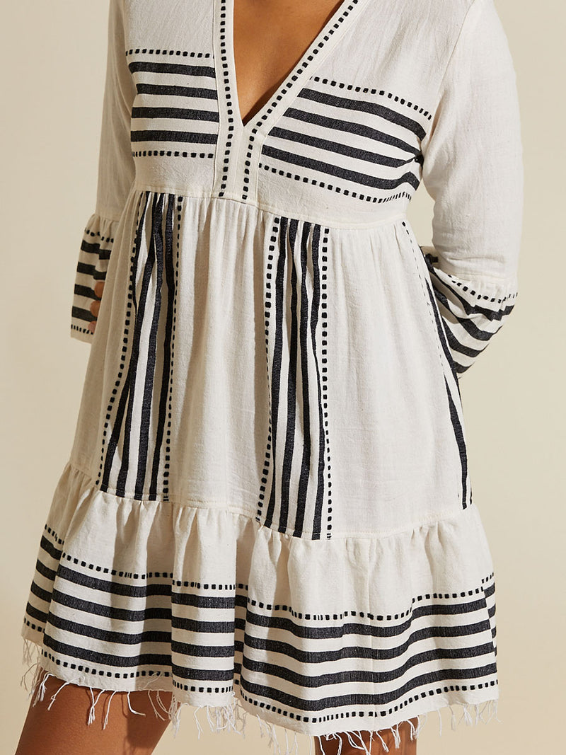 Close up on the chest of a woman standing  wearing the Eshe Flutter Dress featuring architectural and textured black stripes and dotted lines on an off white background.