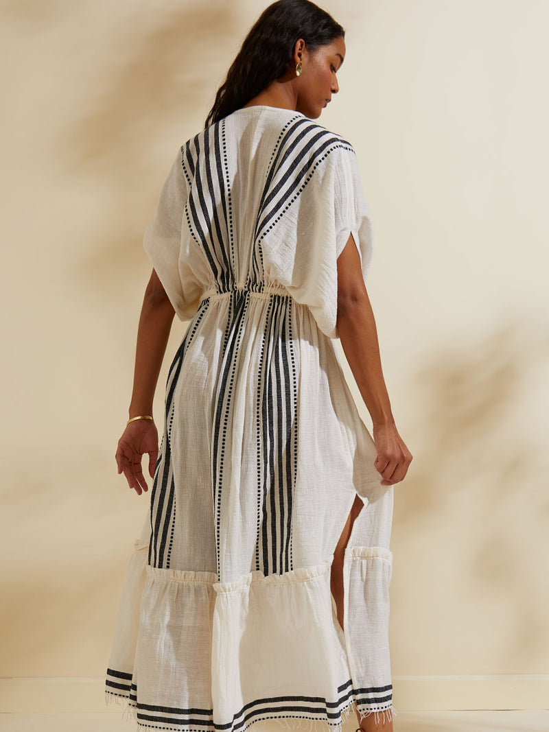 Back view of a woman standing wearing the Eshe Plunge Neck Dress featuring architectural and textured black stripes and dotted lines on an off white background.