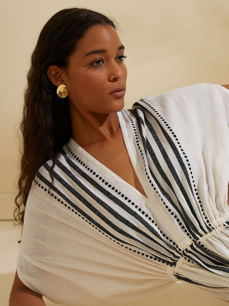 Close on the chest of a woman lounging wearing the Eshe Plunge Neck Dress featuring architectural and textured black stripes and dotted lines on an off white background.