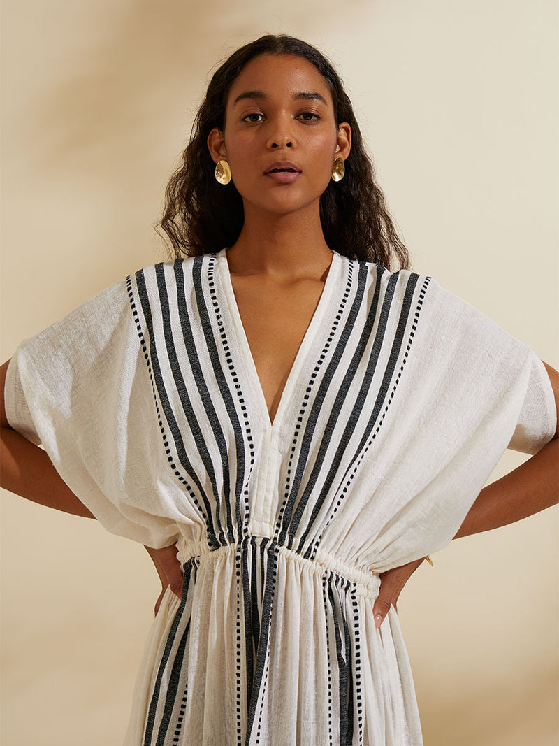 Woman standing with her hands on her hips wearing the Eshe Plunge Neck Dress featuring architectural and textured black stripes and dotted lines on an off white background.