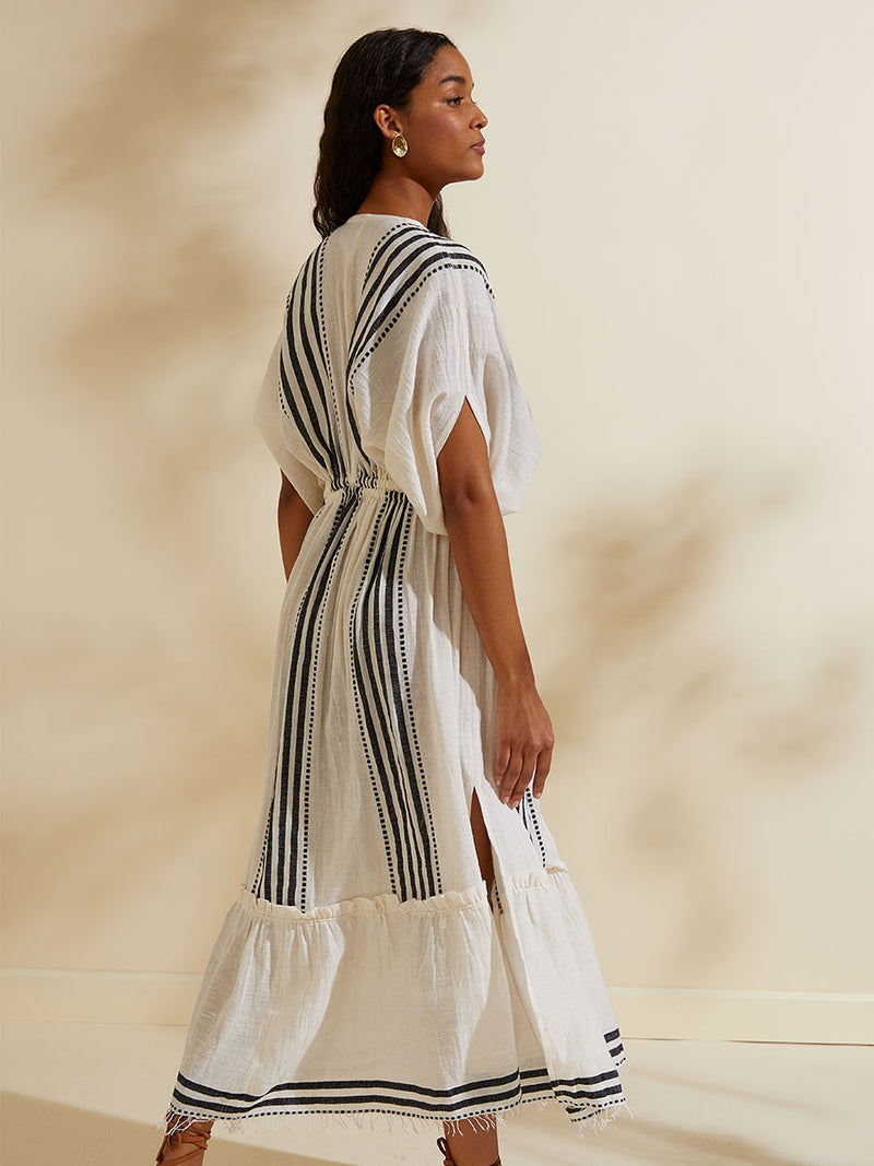 Side view of a woman walking wearing the Eshe Plunge Neck Dress featuring architectural and textured black stripes and dotted lines on an off white background.