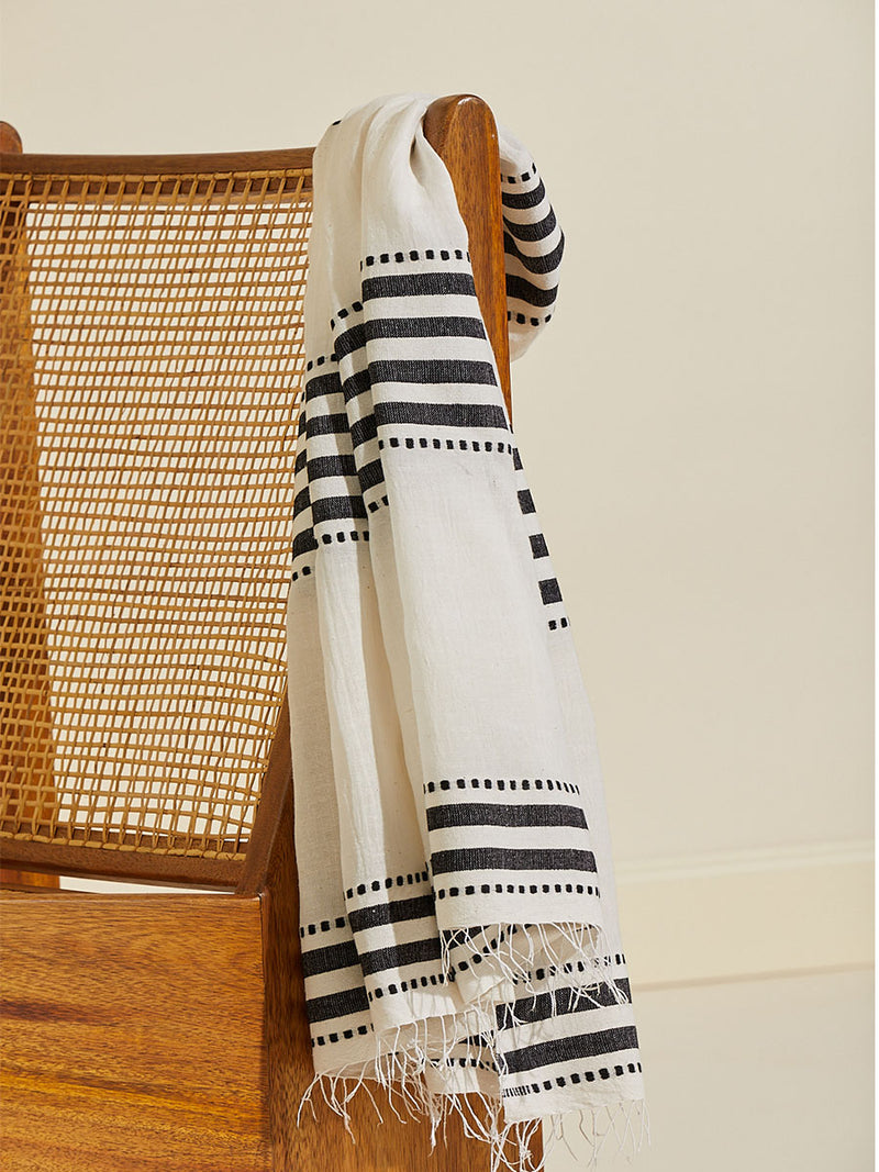 Eshe Sarong hanging on the side of chair featuring architectural and textured black stripes and dotted lines on an off white background.