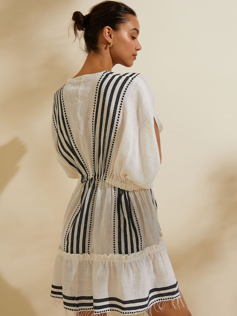 Back view of a woman wearing the Eshe Short Plunge Neck Dress featuring architectural and textured black stripes and dotted lines on an off white background.