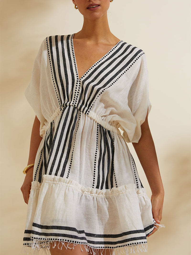 Woman standing wearing the Eshe Short Plunge Neck Dress featuring architectural and textured black stripes and dotted lines on an off white background.