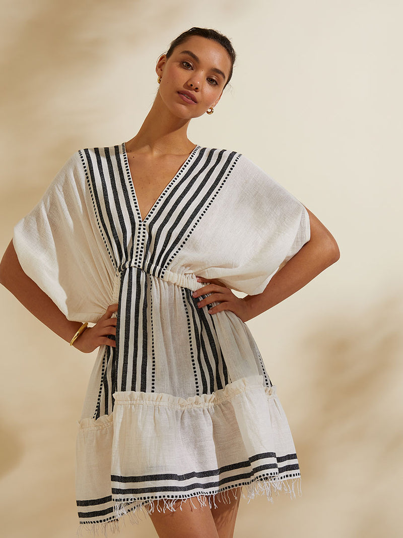 Woman standing with her hands on her hips wearing the Eshe Short Plunge Neck Dress featuring architectural and textured black stripes and dotted lines on an off white background.
