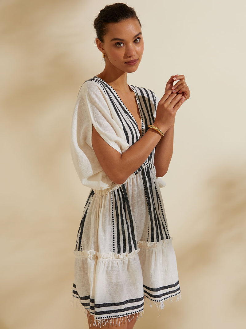 Woman standing holding her hands wearing the Eshe Short Plunge Neck Dress featuring architectural and textured black stripes and dotted lines on an off white background.