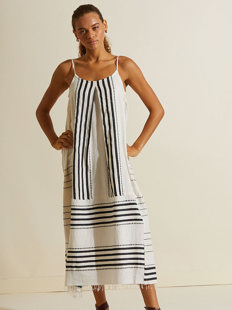 Woman standing with her hands on her hips wearing the Eshe Slip Dress featuring architectural and textured black stripes and dotted lines on an off white background.