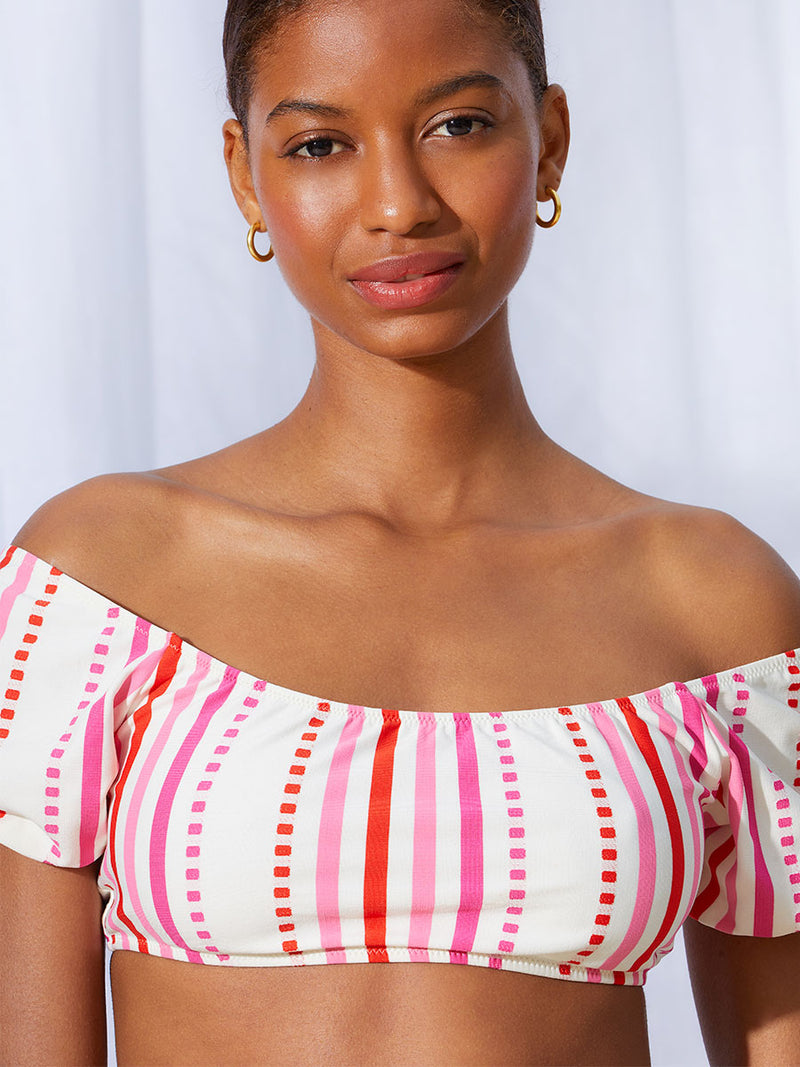 A close up view of a woman standing wearing the Eshe Pouf Top in pink featuring pink stripes and dots pattern and matching side tie bottom.