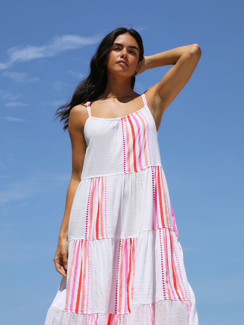 A woman standing wearing the Eshe Cascade Dress in pink featuring pink stripes and dots pattern.