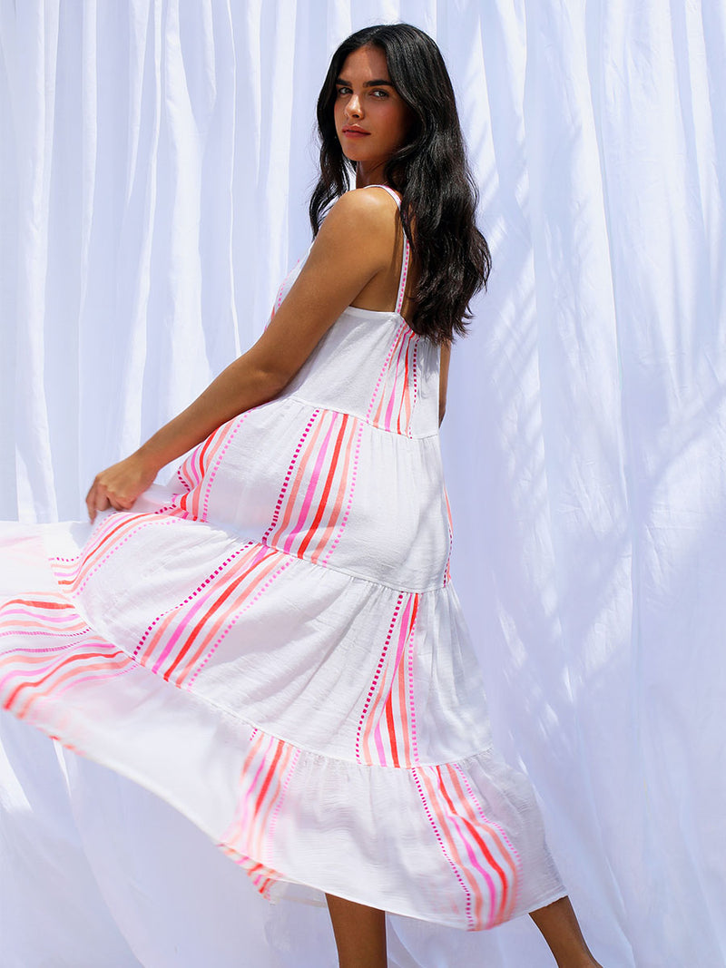 A woman standing wearing the Eshe Cascade Dress in pink featuring pink stripes and dots pattern.