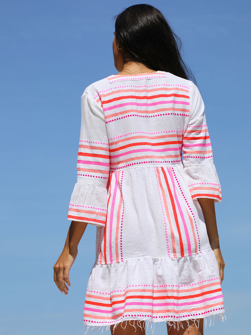The back view of a woman standing wearing the Eshe Flutter Dress in pink featuring pink stripes and dots pattern.